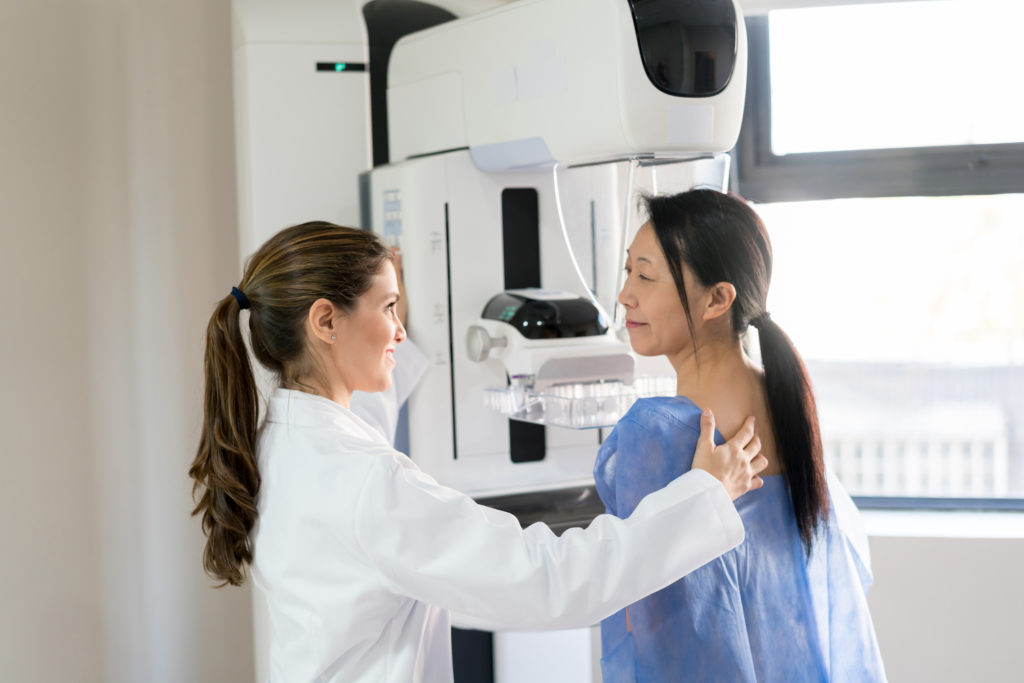 Friendly female doctor talking to her patient and adjusting her position to do a mammogram at the clinic