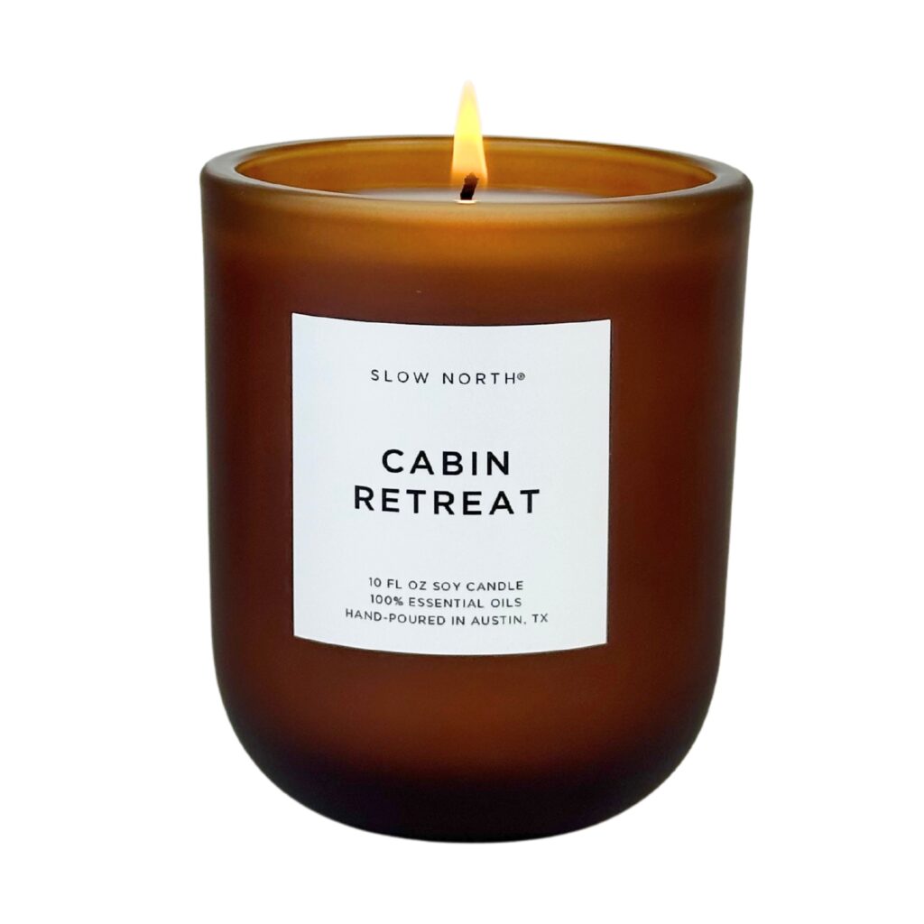 Picture of the Cabin Retreat candle, brown glass container with a rounded bottom shape, white rectangular label in middle with product description