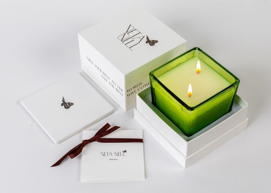 Photo of Veta Nell candle outside of its packaging. Candle comes in a white cube box with Veta Nell branding. candle is in a cubed translucent green container with two wicks.