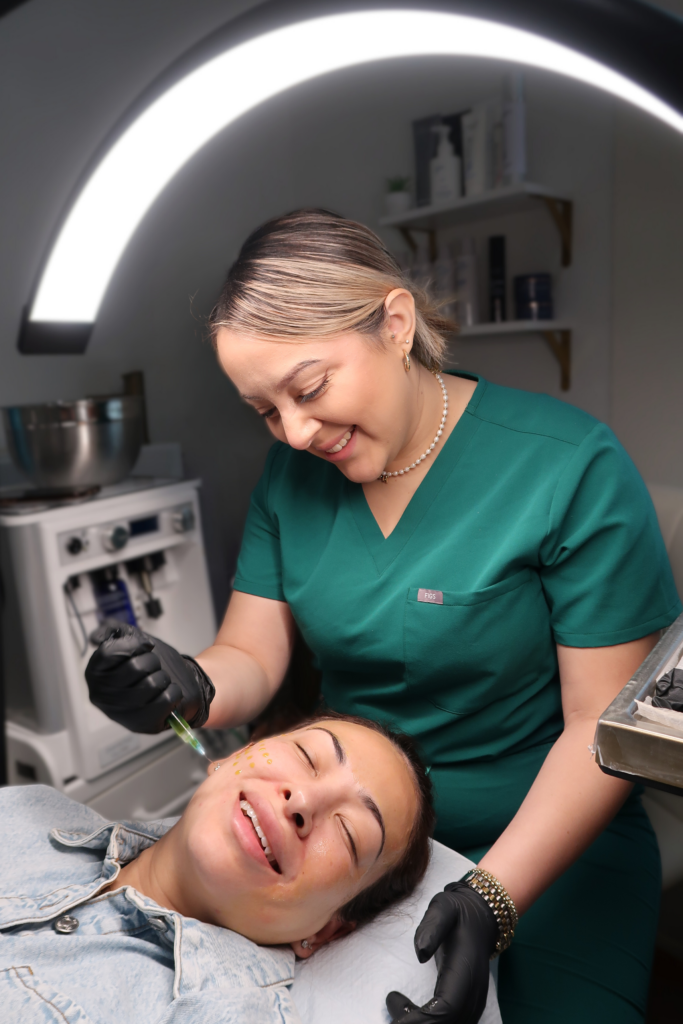 Photo of aesthetician wearing green scrubs working with a patient lying down in the aesthetics studio .