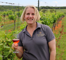 Julie Kuhlken standing in the vineyard holding a glass of her Perdernales Cellars wine.