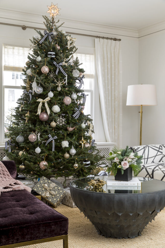 A holiday tree in a living room dressed with decorative balls of pearly pinks, white and silver along with gold and white bows with wrapped gifts under the tree.